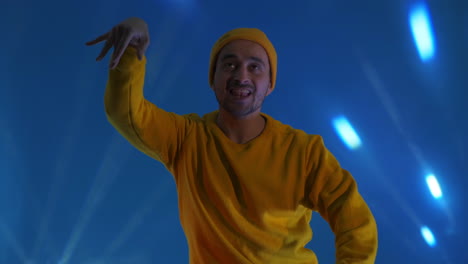 Smiling-man-dancing-in-studio.-Joyful-guy-gesturing-with-hands.-Man-having-fun.-man-smiling-and-dancing-challenge-dance-in-good-mood-on-blue-background.Unstoppable-fun-happiness-comical-portrait.